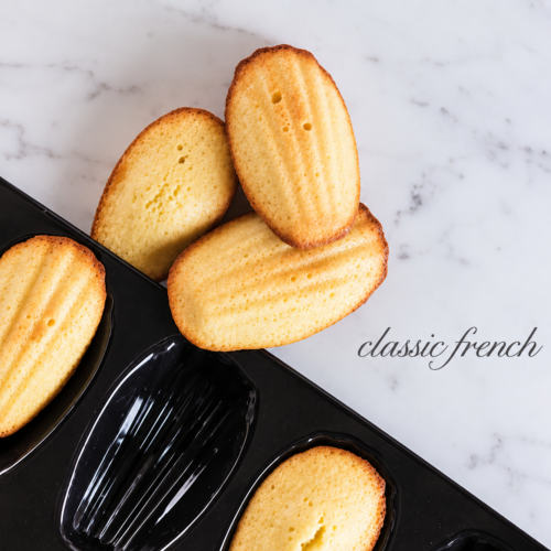 Classic French madeleines baked in a black FORTEEZ Madeleine Tray on a white marble surface.