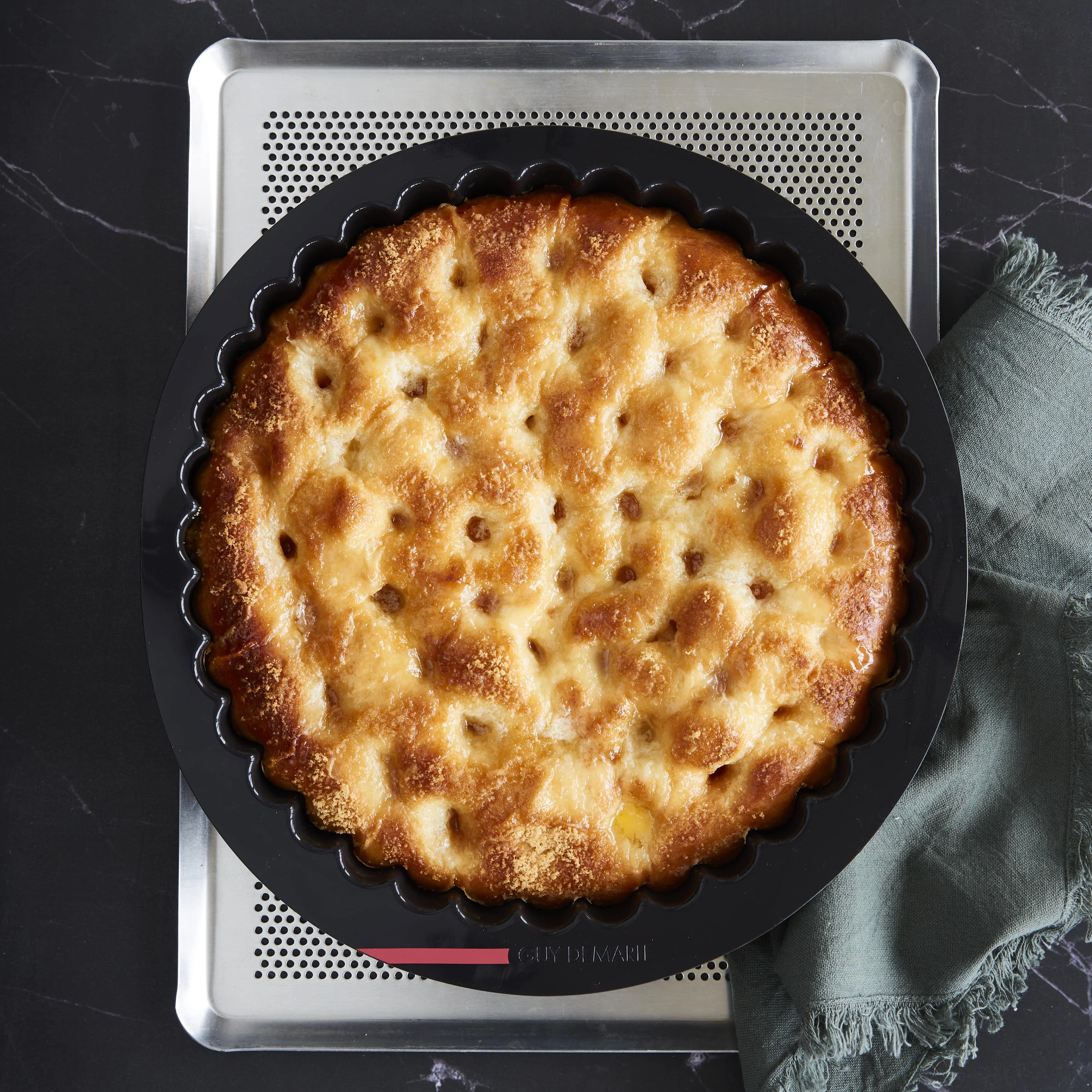 Overhead view of golden baked bread in a black Guy Demarle fluted silicone mold on a perforated baking sheet.